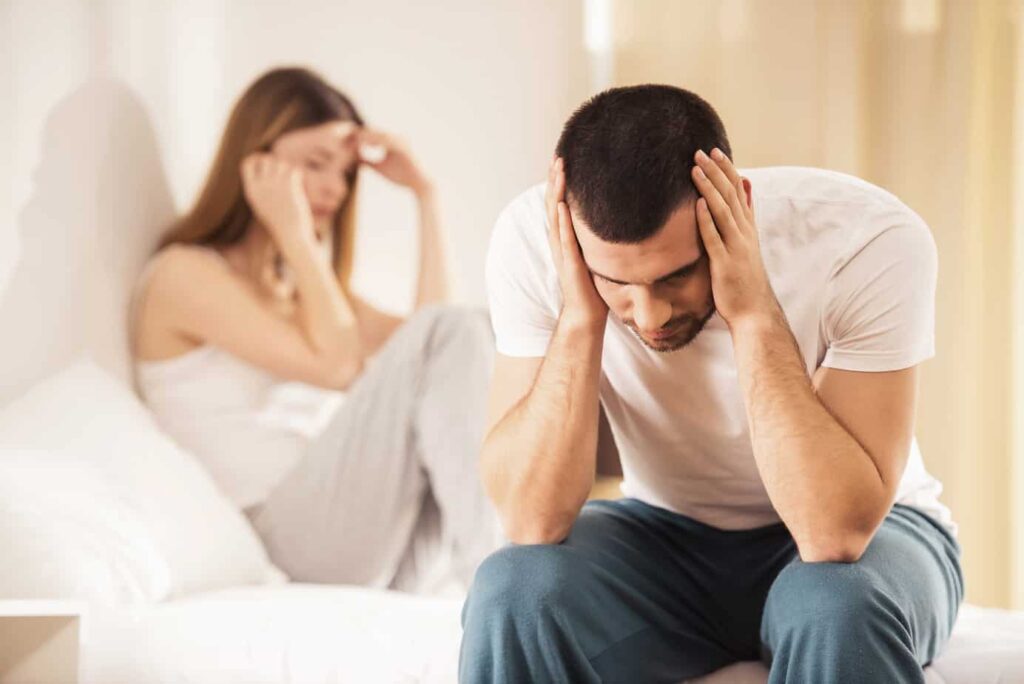 a young couple sat on opposute sides of the bed considering divorce