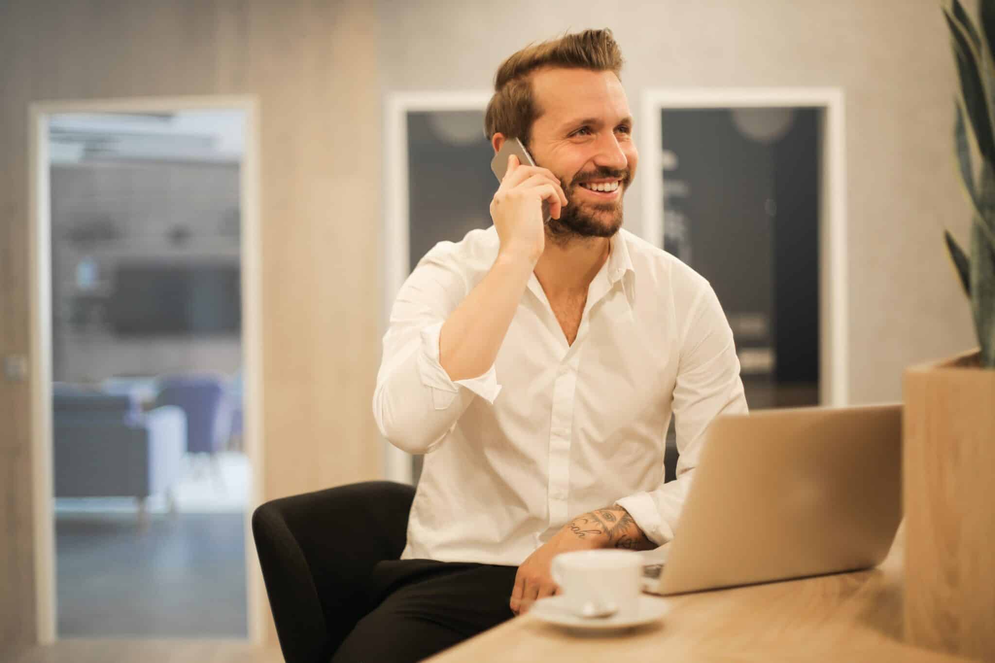 happy client smiling on the phone in front of computer with a coffee