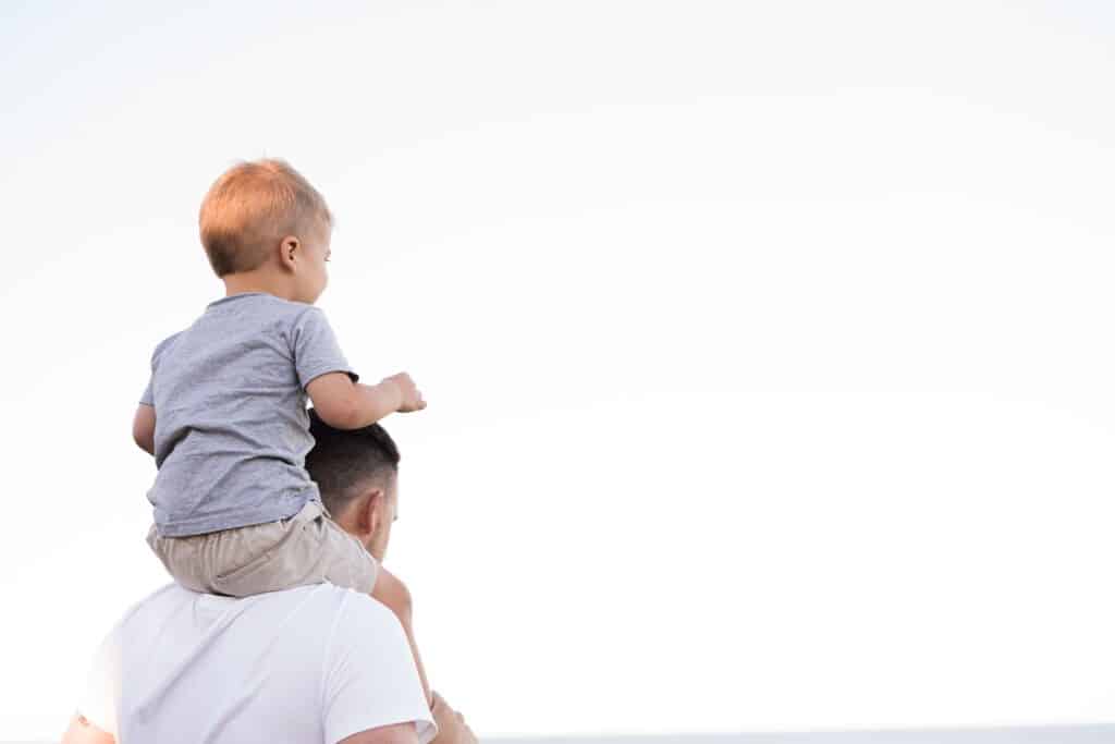 man walking on the beach with his son on his shoulders