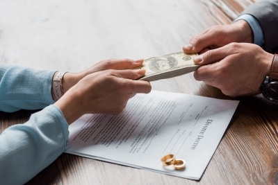 cropped shot of lawyer and client holding dollar banknotes above divorce decree with wedding rings